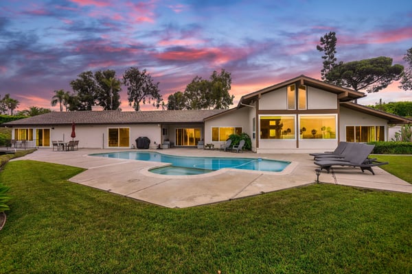 Modern white house with pool and patio at sunset, palm trees and manicured lawn visible